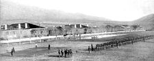 A black and white picture of Fort Grant near Stafford, Arizona circa 1885. Center middle ground to right middle ground is about four or five companies of soldiers standing in ranks. The buildings of the Fort in the background.