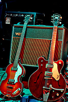 Two electric guitars, a light brown violin-shaped bass and a darker brown guitar resting against a Vox amplifier