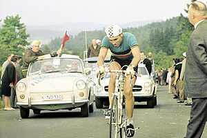 A man on a bicycle, with a car behind him.