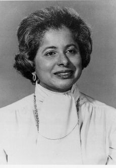 Woman with greying dark hair wearing a white turtleneck