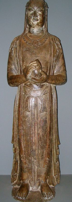 A standing Buddha: a yellow statue made from limestone, with its hands in prayer and holding a lotus