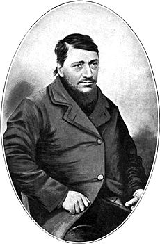 A confident-looking man of about 40 with a large dark beard. The thumb on his left hand is conspicuously absent.