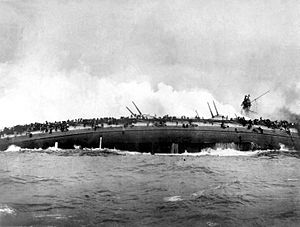 The burning hull of a ship on its side; water pours from holes punched by enemy projectiles. The keel is splitting from the intense strain.