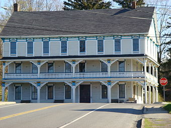 A three-story white building with a full-length second-story balcony, blue trim and a black roof