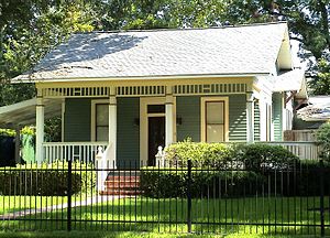 Small, single-story structure with pitched roof. A center door is flanked by a window on each side. Wide stairs lead to a wide, front porch with wood railing.