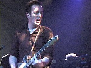 A photograph of Joe Strummer playing his guitar while performing at St. Ann's Warehouse in Brooklyn, New York City on 5 April 2002.