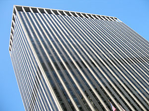 Street view of top half of skyscraper against the sky; its outside is dominated by vertical black and white lines