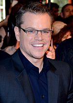 A man is wearing a navy blue collared shirt and glasses.