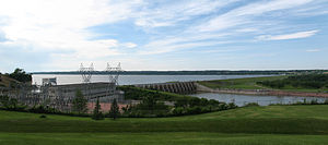 Side view of a dam surrounded by green hills under a clear sky