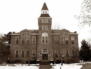 Apparent two or three story building with central tower in front; roof contains several skylights