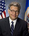 Head and shoulders portrait of man in his forties with close-gray hair in a business suit and tie with a U.S. and Minnesota flag in the background