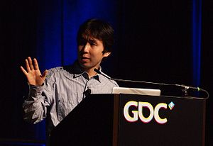 A Japanese man gestures in front of a podium.