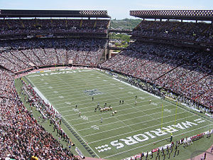 A football field with players lined up in the middle of it surrounded by a packed stadium