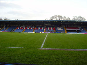 Bury's blue stadium seated stand covered in red, white and black F.C. United banners.