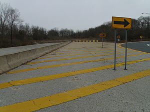 A freeway coming to a blocked-off dead end in a wooded area, with a right arrow sign pointing motorists onto an off-ramp