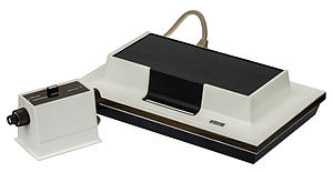 Photograph of a dedicated video game console with two input devices connected to it with cables.