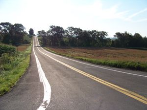 A two-lane highway passes amongst open fields in a rural area.