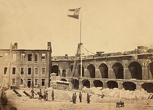 1861 photograph of the interior of a damaged military fortification. The flag of the Confederate States of America flies from a flagpole near the center of the photograph.