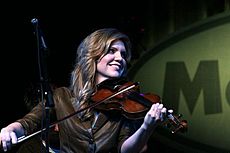 A woman wearing a brown jacket and playing a fiddle.