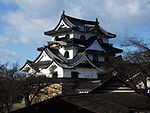 A castle with white walls, dark roofs and many gables on a platform of unhewn stones.