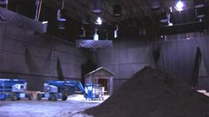 A studio sound stage, with a pile of mulch in the foreground and cherry pickers and a constructed mausoleum in the background.