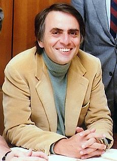 Color photo. Man sitting wearing a suit and smiling.