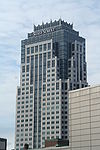 Fround-level view of an ornate building with alternating concrete and blue-tinted glass facades. Near the building's roofline, a sign with the words "STATE STREET" is visible. Capping the building is a crown-like structure composed of blue glass and white spires.