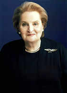 Madeline Albright wearing a dark blouse and coat, with an eagle badge on her left shoulder