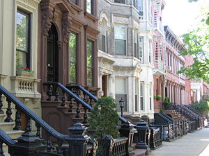 A view down a street with rowhouses in brown, white, and various shades of red.