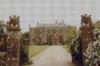 Yellow stone building at the end of a driveway accessed via stone gateposts.