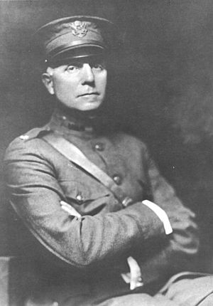 A black-and-white image of a man sitting in a chair in a full military uniform