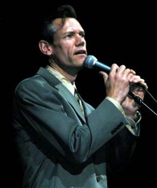 A man in a black suit clutching a microphone