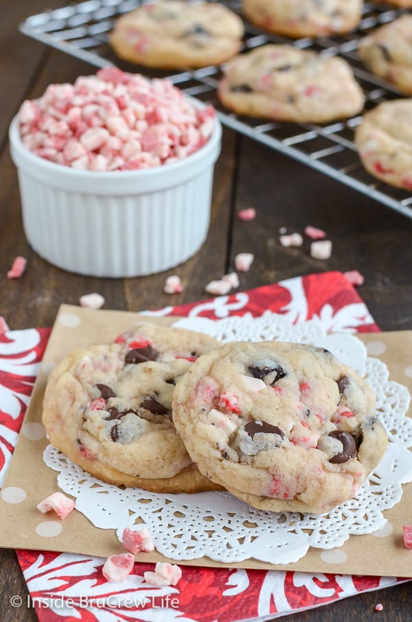 Two Oreo peppermint crunch cookies on a white doily with a bowl of peppermint chips behind them