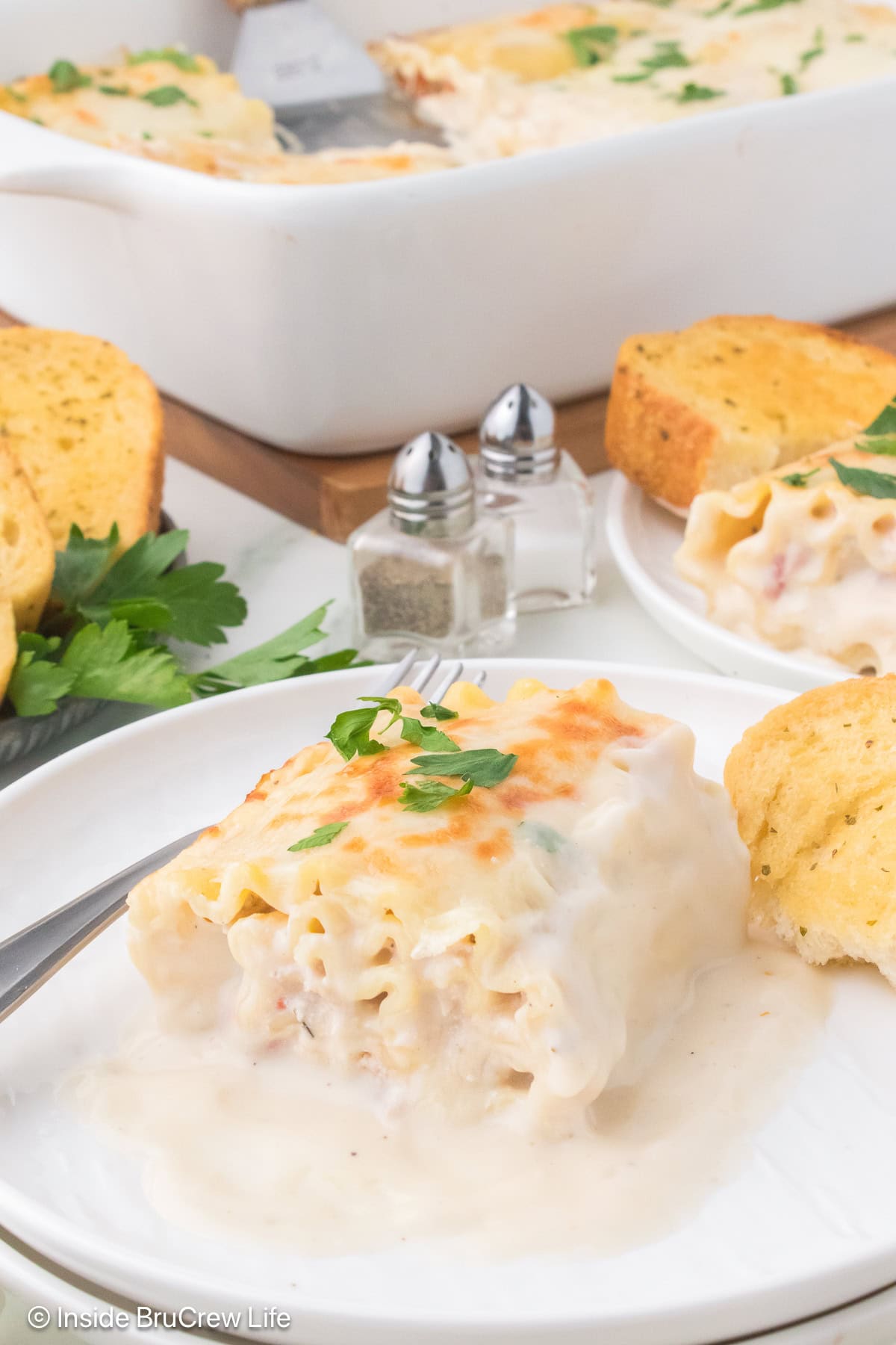 A white plate with a creamy Alfredo lasagna roll up on it.