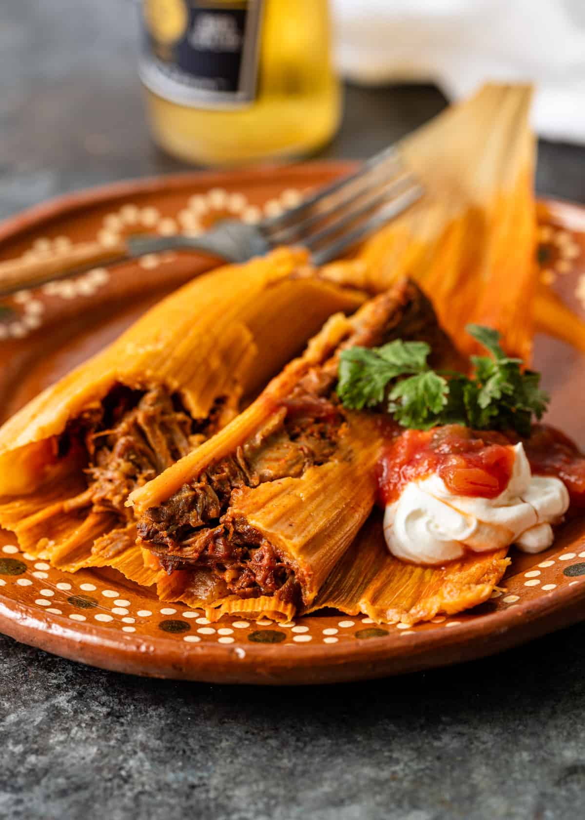 pork tamales on an orange ceramic plate with sour cream, salsa, and fresh herbs on top