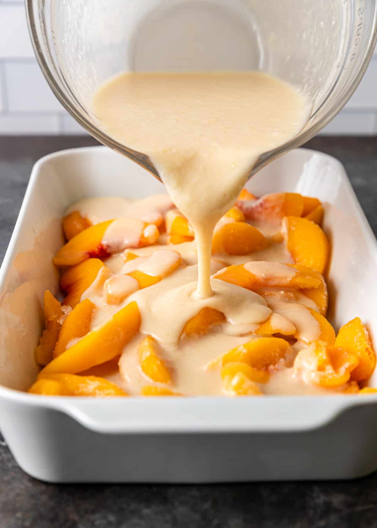 overhead: pouring the cobbler batter over fresh peaches in a baking dish