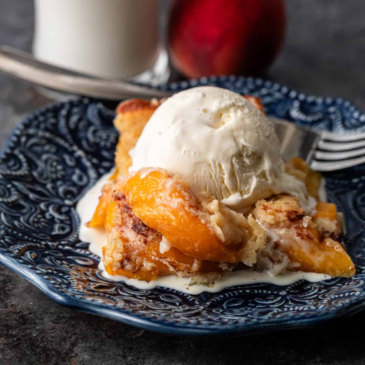 a large slice of peach cobbler with vanilla ice cream on top on a blue plate