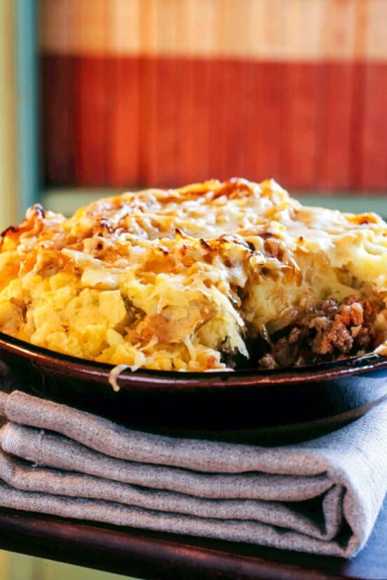 A porcelain bowl filled with shepherd's pie and topped with potatoes, onions, and cheddar.