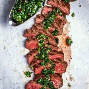 A sliced steak chimichurri with a gravy boat filled with chimichurri on the side.