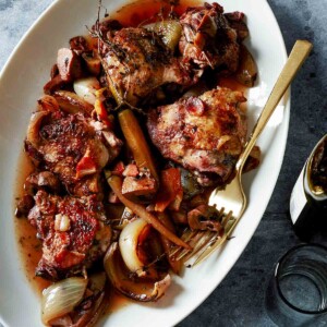 A white oval serving plate filled with slow cooker coq au vin and a gold fork resting on the side of the plate.