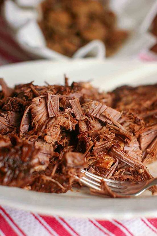 A plate of shredded Coca-Cola brisket with a fork resting in the meat.