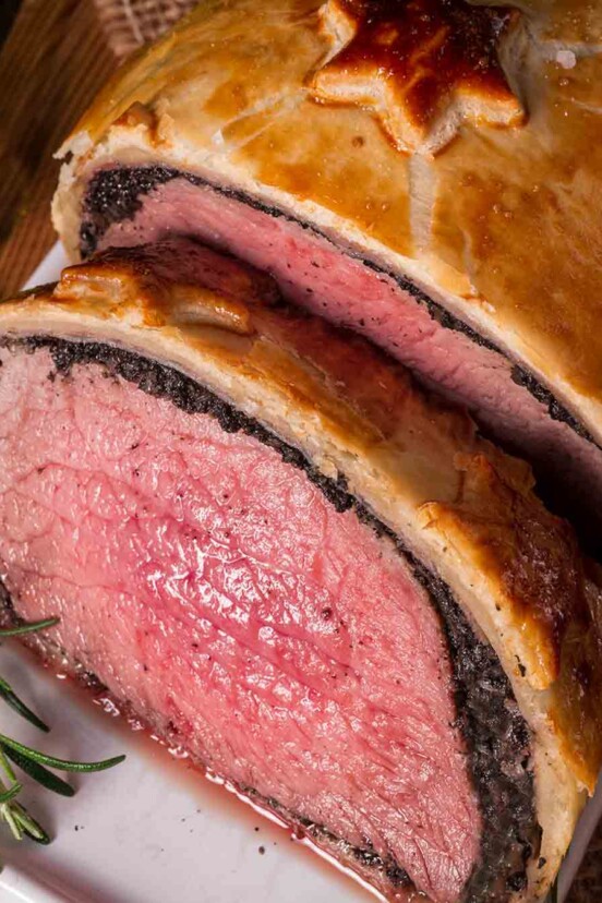 Close-up of a beef Wellington on a plate with a sprig of rosemary