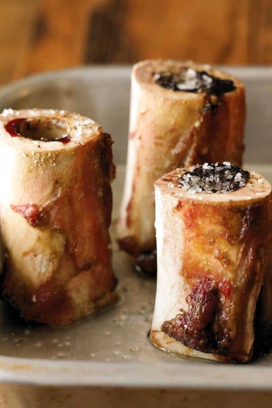 Three pieces of roasted bone marrow sprinkled with salt in a metal roasting pan.