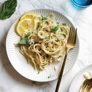 Two white plates topped with lemon basil pasta with lemon slices on the side and a gold fork resting on the side of each plate.