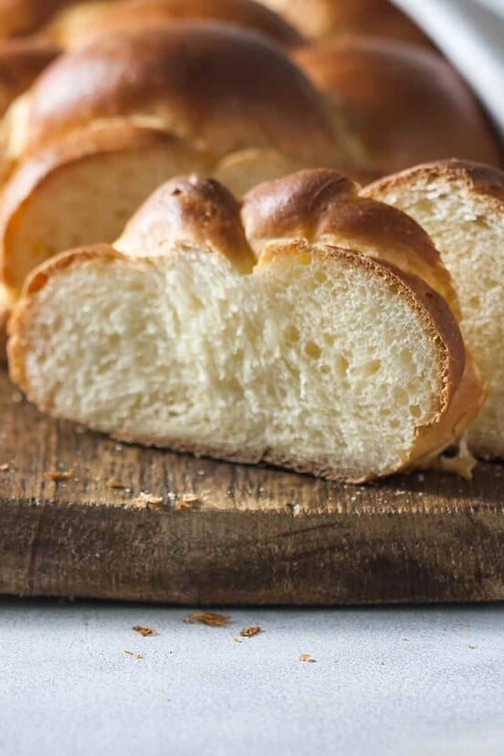 A partially sliced loaf of challah on a wooden cutting board.