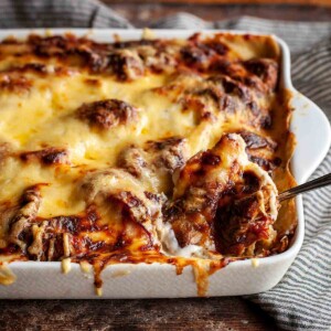 A finished croque monsieur casserole in a white baking dish with a spoon resting inside.