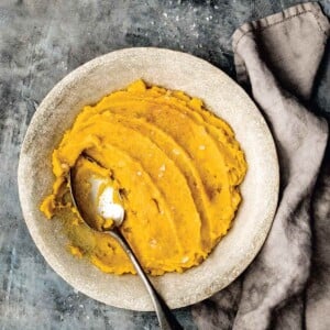 A ceramic bowl filled with mashed kabocha with a spoon resting in it.