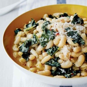 A bowl of white beans and Tuscan kale, sprinkled with grated Parmesan cheese, with a spoon.