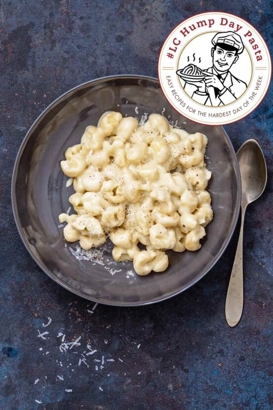 Skillet mac and cheese in a grey bowl with a spoon, garnished with extra shredded cheese.