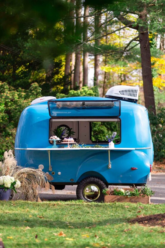 A blue trailer in the woods, with desserts on a shelf.